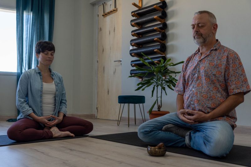 Hombre y mujer meditando en una sala con esteras de yoga.