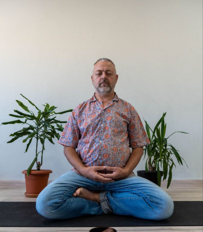 Hombre meditando en posición de loto en una sala con plantas.